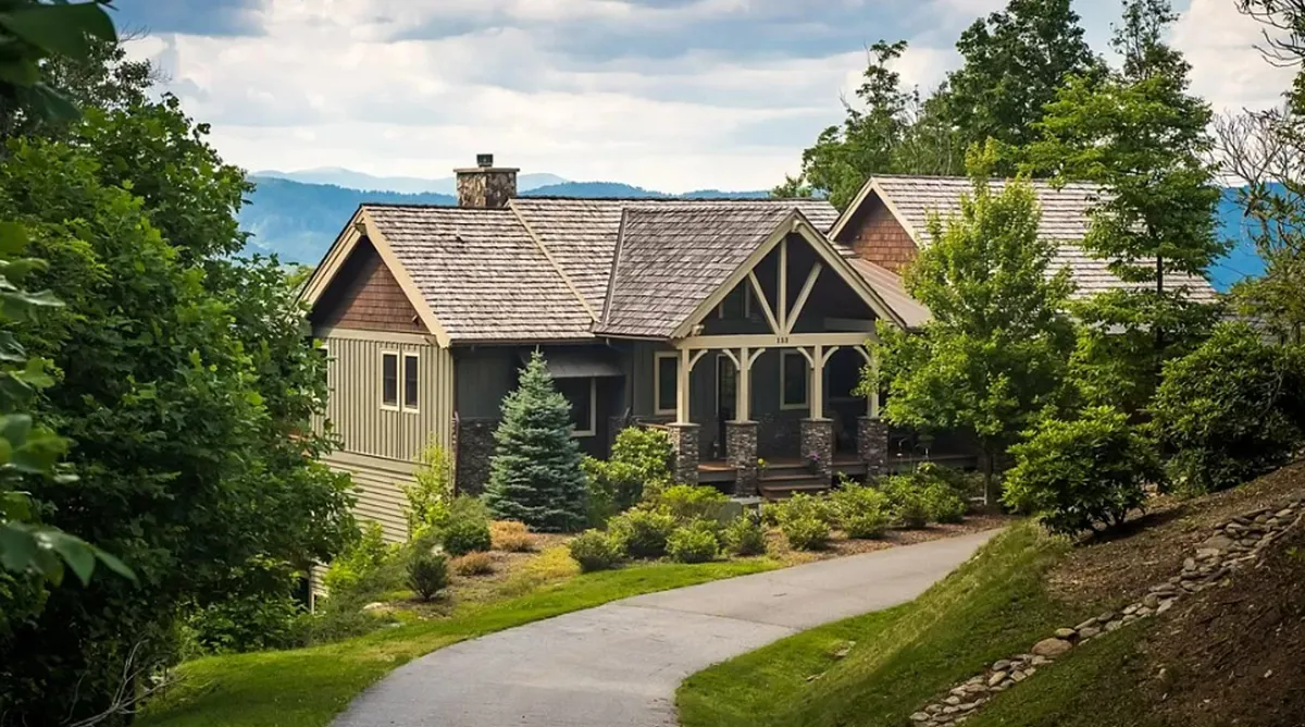 The hero image shows the Blue Hole Lodge’s inviting exterior surrounded by lush landscaped gardens, with a winding pathway leading up to a spacious porch—set against the tranquil backdrop of the Blue Ridge Mountains. The scene evokes a sense of peaceful seclusion and natural beauty, perfect for enjoying morning coffee or unwinding after a day of adventure.