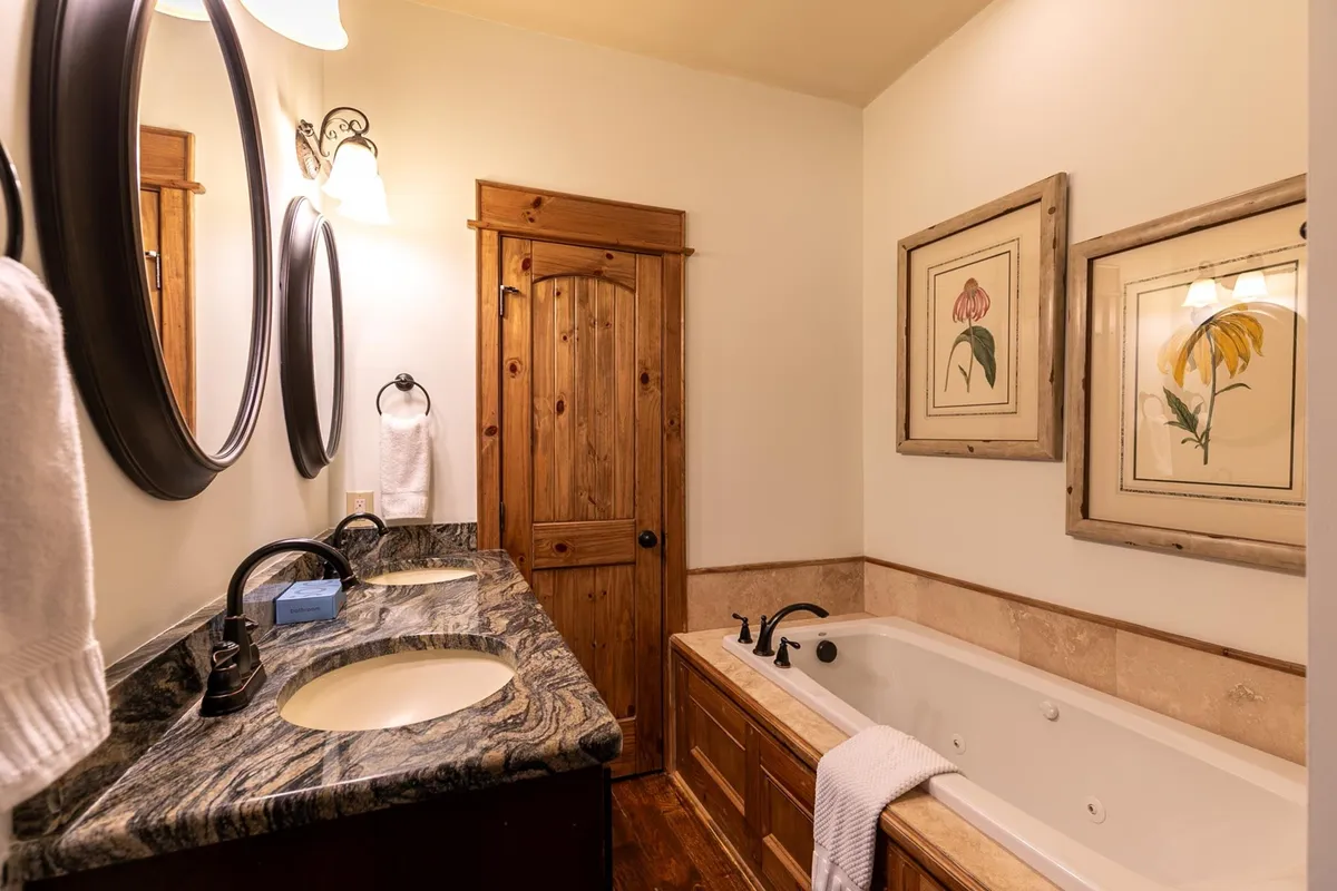 A spacious bathroom featuring a double sink vanity, large mirrors, a deep bathtub, and framed floral artwork. The mood is calm and rejuvenating, evoking a spa-like experience.