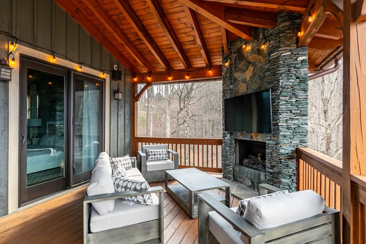This exterior image shows a cozy outdoor seating area with a stone fireplace, a TV mounted above, and a wooden ceiling overhead—creating an inviting spot for relaxing, entertaining, and group activities.