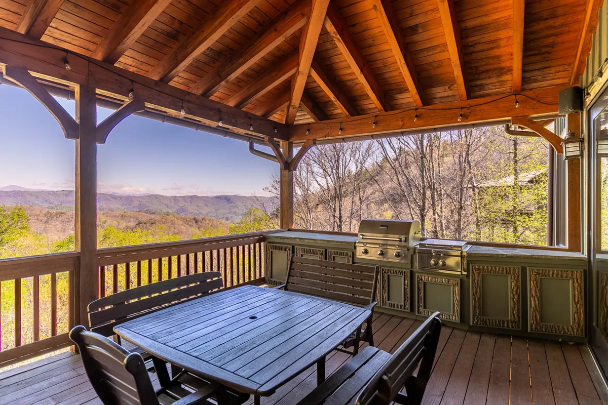 A wooden deck set against a panoramic mountain backdrop, complete with a dining table and an outdoor grill. The scene is primed for alfresco dining, barbecuing, and soaking in expansive Blue Ridge vistas, reflecting a relaxed and sociable atmosphere.