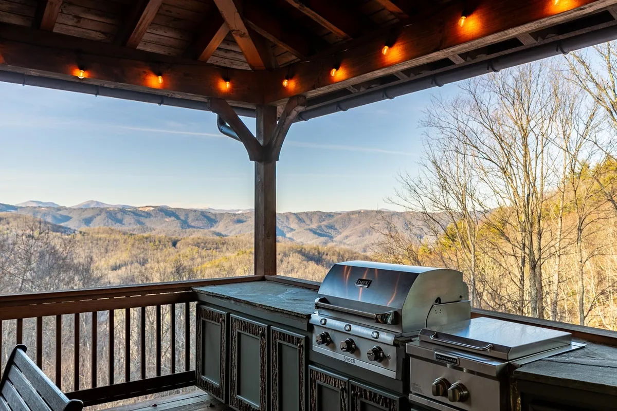 This exterior image features an outdoor grill area set against a backdrop of stunning mountain views and a wooden deck structure, inviting guests to cook, dine, and relax while surrounded by nature.