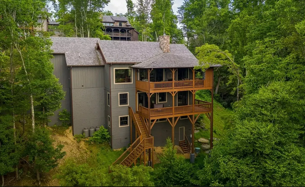 An exterior view highlighting a wooden deck with railings overlooking the forest, set against a backdrop of lush trees and the multi-level structure of the lodge. The peaceful deck invites relaxation or preparation before heading out to explore the natural surroundings.