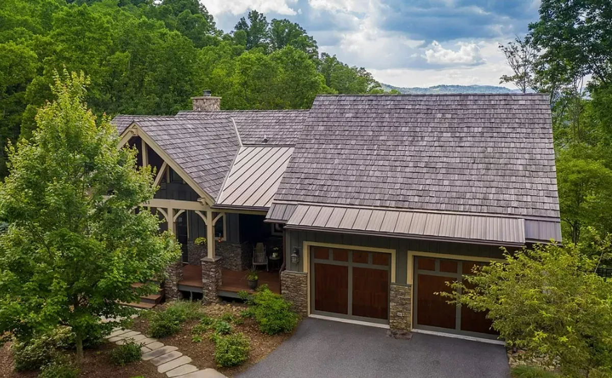 The welcoming exterior view featuring a spacious front porch with double garage doors, stone accents, and vibrant greenery. The porch's ample space is perfect for group gatherings or relaxing after exploring the local culinary scene.