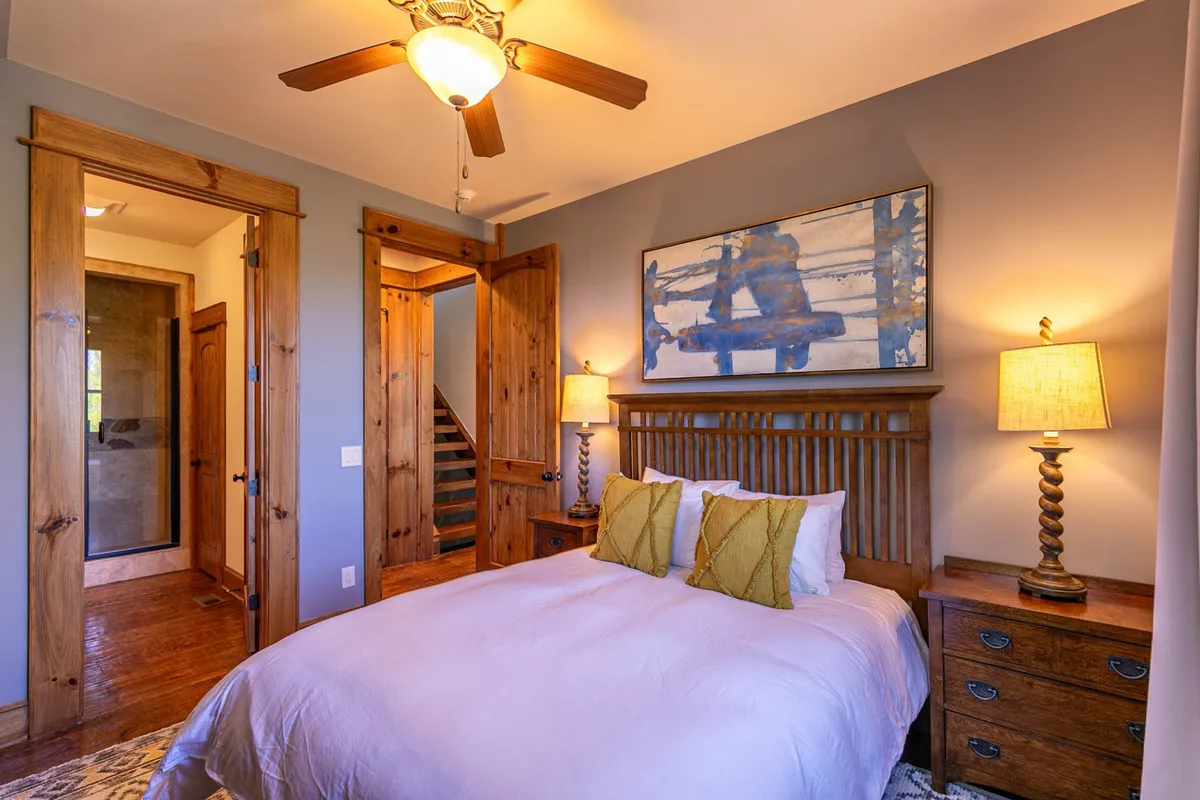 A peaceful guest bedroom with a bed dressed in white linens and green accent pillows, wooden nightstands with soft lighting, and large artwork on the wall. The atmosphere is tranquil and comfortable, ideal for restful sleep.