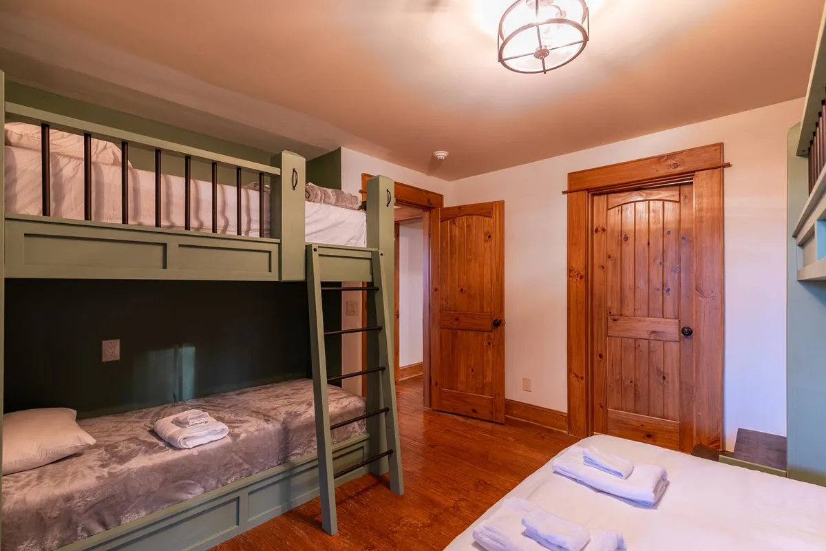 A welcoming bunk room featuring charming wooden bunk beds, textured walls, and wooden doors. The room exudes a playful yet cozy mood, ideal for both children and adults. It feels like a space designed for family bonding and cherished memories.