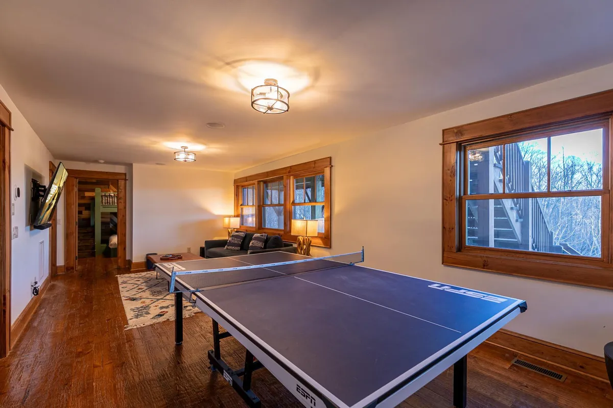 Inside, a game room featuring a ping pong table, a comfortable sofa, and large windows creates an upbeat, playful atmosphere perfect for friendly tournaments and family laughter.