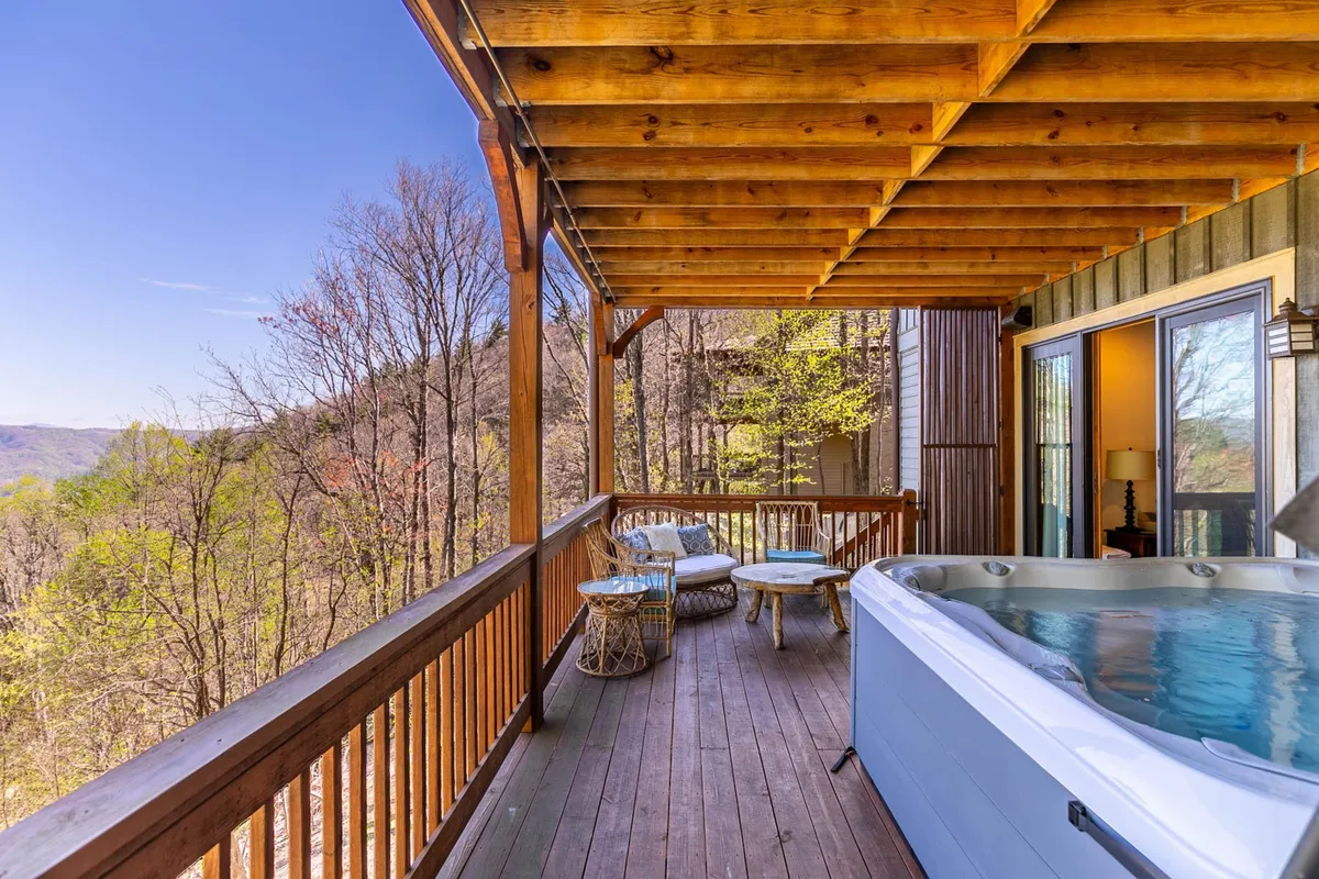 A tranquil outdoor scene featuring a hot tub and seating area framed by wooden beams, set amidst natural landscape views. The surrounding forest and open sky establish a strong connection to nature and the outdoors, inviting relaxation after a day of adventure.