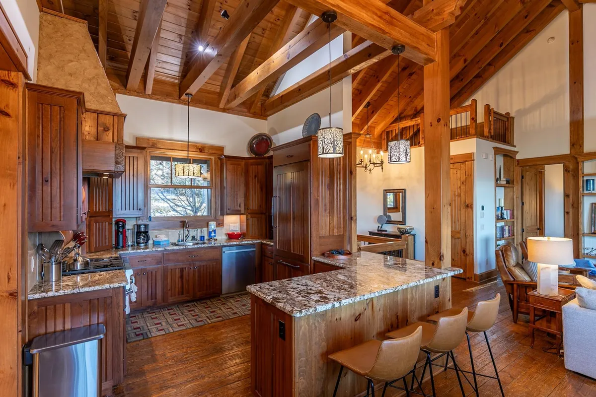 A bright, open-concept kitchen interior with granite countertops, wooden cabinetry, high wooden beams, and an inviting dining area. The kitchen is well-equipped for preparing feasts or casual breakfasts with family and friends.