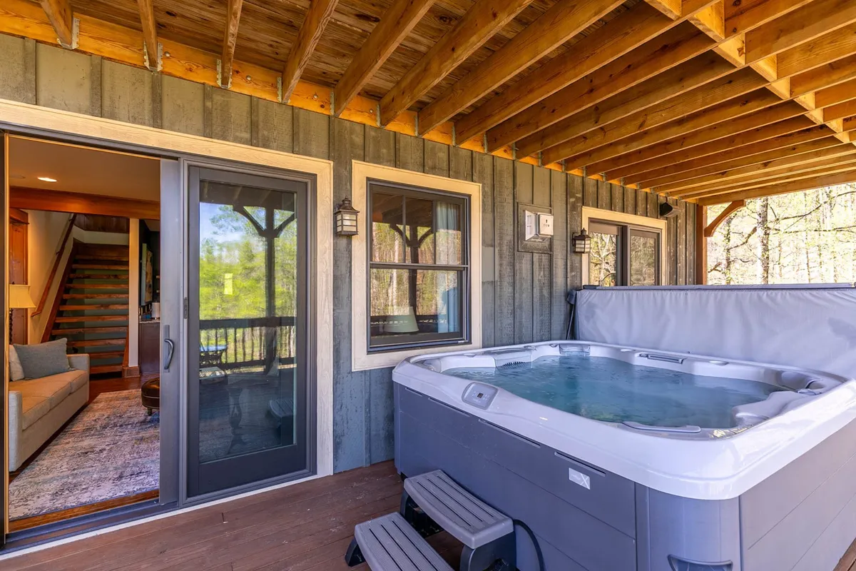 An inviting exterior shot featuring a private hot tub on a wooden deck, with panoramic sunset views of the mountains. The setting is tranquil, ideal for couples or friends seeking relaxation after a day of adventure.