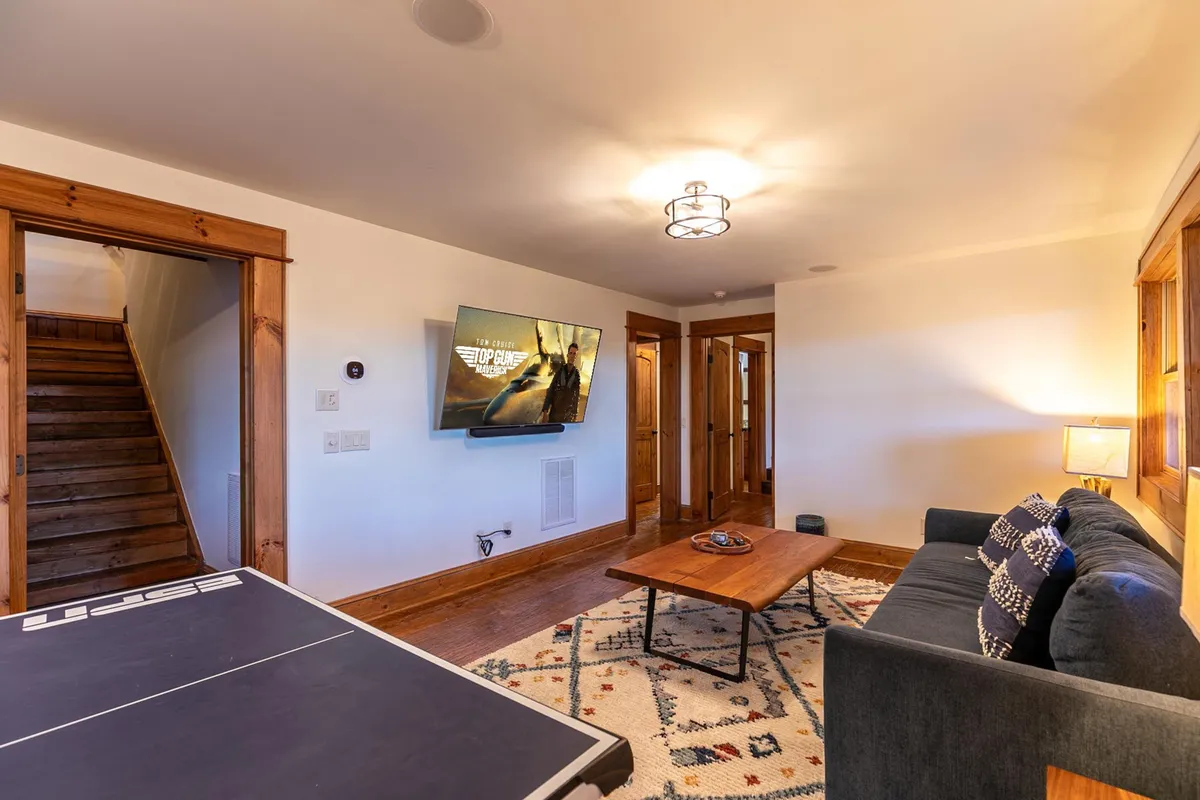 This image showcases a lively game room with a ping pong table at its center, a plush sofa, a television on the wall, and a coffee table nearby. The room's casual layout and entertainment-focused furnishings invite both competitive play and relaxed lounging, making it ideal for gatherings and game nights.