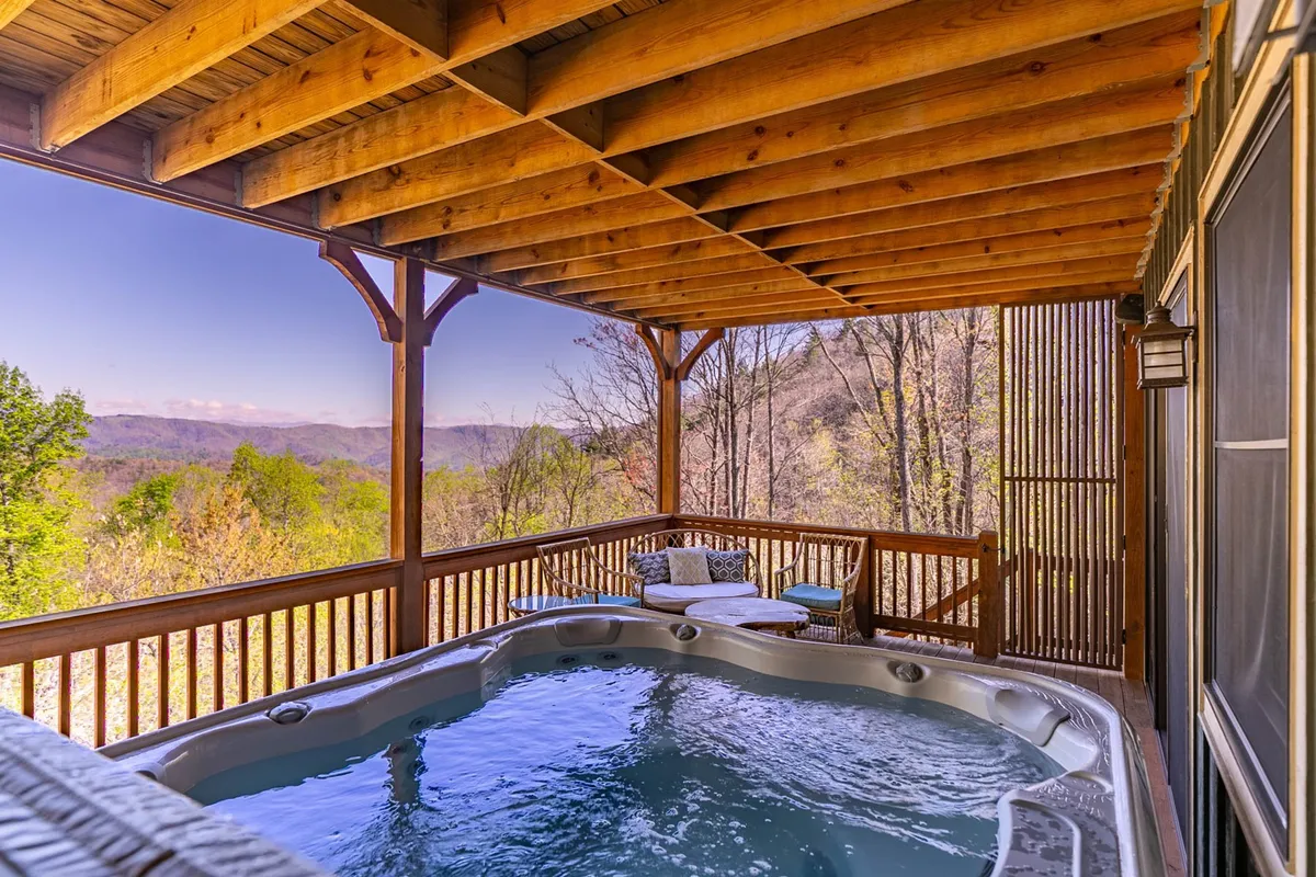 An exterior hot tub is set against a spectacular mountain backdrop, with comfortable seating on the surrounding deck. The bubbling water and panoramic views create a tranquil atmosphere, inviting guests to relax after indoor activities.